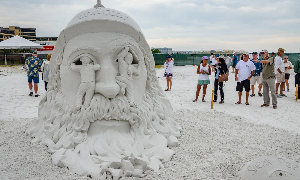 crowd on the beach admiring a large sand sculpture